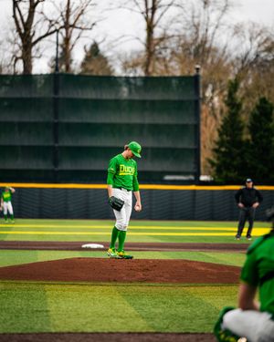 Oregon Ducks pitcher stands on the mound in bright green uniform during a college baseball game on an overcast day.