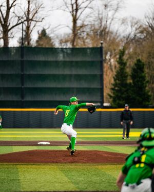 Oregon Ducks pitcher in green uniform winds up to throw on the mound during a college baseball game.