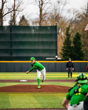 Oregon Ducks pitcher in green uniform delivers a pitch during a college baseball game on a well-maintained field.