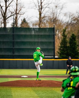 Oregon Ducks pitcher in green uniform winds up on the mound during a college baseball game.