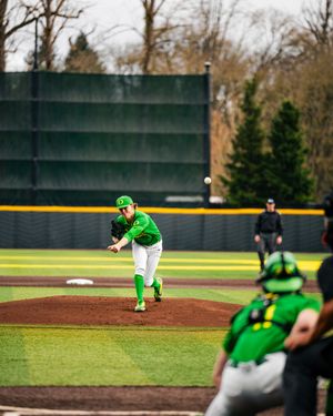 Oregon Ducks pitcher in green uniform delivers a pitch during a college baseball game on a cloudy day.