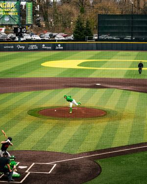 Oregon Ducks pitcher delivers a pitch at an NCAA baseball tournament game in a lush green stadium.