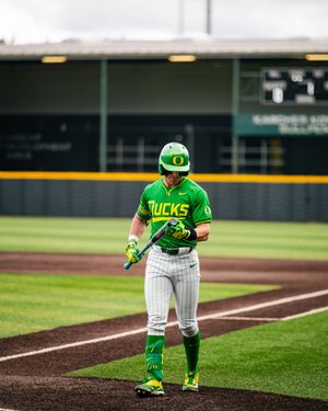 Oregon Ducks baseball player in green uniform holding bat on field during game at PK Park stadium.