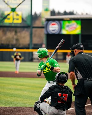 Oregon Ducks baseball batter in green helmet at home plate with catcher and umpire during a college baseball game.