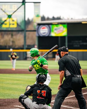 Oregon Ducks batter in green uniform at home plate during a college baseball game with umpire and catcher.
