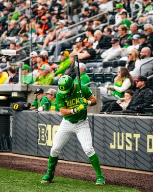Oregon Ducks baseball player in green uniform batting at home plate during a college game at a packed stadium.