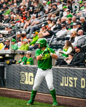 Oregon Ducks baseball player in green uniform stands ready to bat at home plate during a college baseball game.