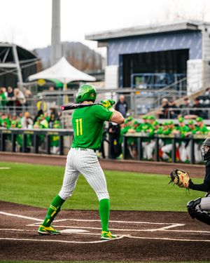Oregon Ducks baseball player #11 in green uniform batting at home plate during a college baseball game.