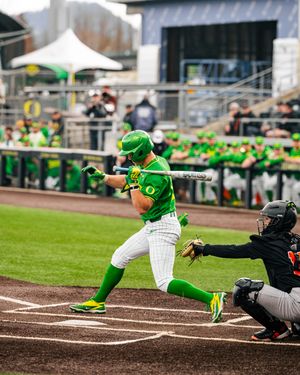 Oregon Ducks baseball player in green uniform swings bat during college game at home plate.
