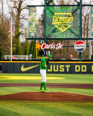 Oregon Ducks pitcher in green uniform winds up on mound at PK Park with Nike and Pepsi signage visible.