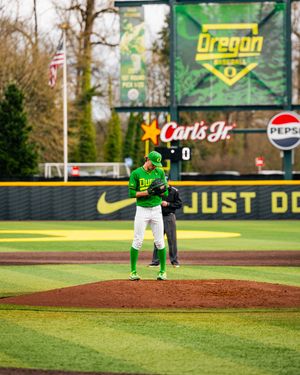 Oregon Ducks pitcher stands on the mound at PK Park baseball stadium with Carl's Jr. and Pepsi ads visible.