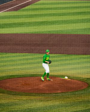 Oregon Ducks baseball pitcher in bright green uniform stands on the mound at a striped outfield stadium.