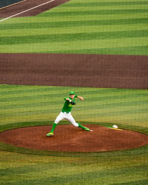 Oregon Ducks pitcher in green uniform winds up on the mound at a well-manicured baseball stadium.
