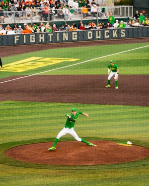 Oregon Ducks pitcher winds up on the mound at a Fighting Ducks baseball game in green and yellow uniforms.