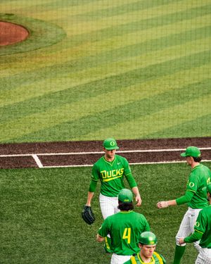 Oregon Ducks baseball players in green uniforms gather on the field during a college baseball game.