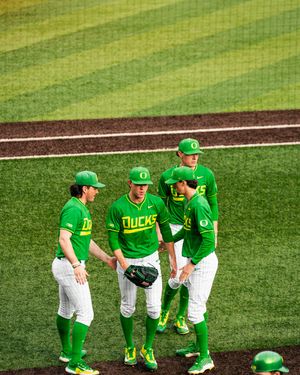 Four Oregon Ducks baseball players huddle on the field in bright green uniforms during a college game.