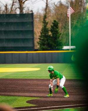 Oregon Ducks softball player in green uniform ready at base during a college game with American flag in background.