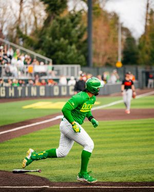 Oregon Ducks baseball player in green uniform running bases during a college game at a packed stadium.