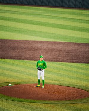 A baseball pitcher in a green Oregon Ducks uniform stands on the mound at a well-manicured baseball stadium.