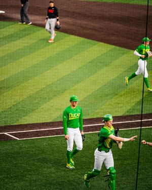 Oregon Ducks baseball players in bright green uniforms warm up on the field during a game.