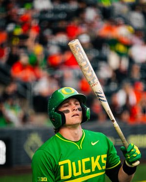 Oregon Ducks baseball player in green uniform holds bat upright at home plate during a college baseball game.
