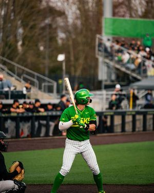 Oregon Ducks baseball player in green uniform batting stance at home plate during a college baseball game.
