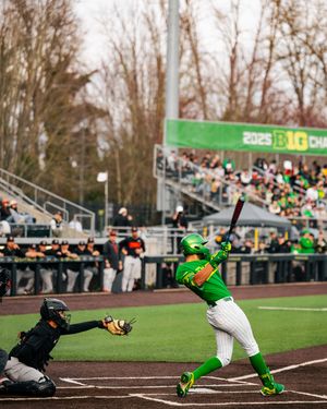 Oregon Ducks batter swings at pitch during 2025 Big Ten college baseball game with catcher and crowd in background.