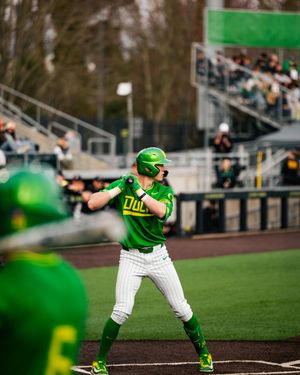 Oregon Ducks softball player in green uniform batting stance at home plate during a college softball game.