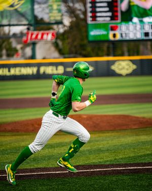 Oregon Ducks baseball player sprints the bases in green uniform at Kilkenny Field during a college game.