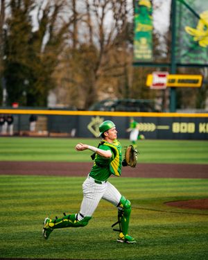Oregon Ducks baseball catcher in green uniform throwing ball during game at Bob Moore Field.
