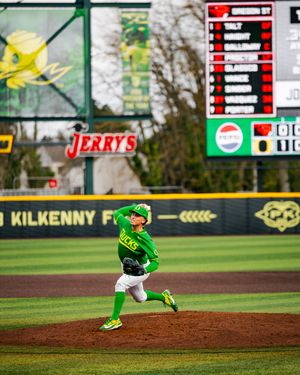 Oregon Ducks pitcher in green uniform delivers a pitch at PK Park baseball stadium during a college baseball game.