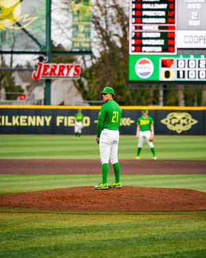 Baseball pitcher #21 in green Oregon Ducks uniform stands on the mound at Kilkenny Field during a college game.