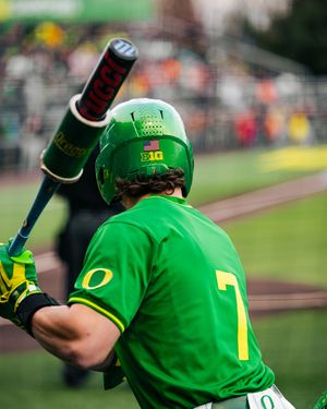 Oregon Ducks baseball player #7 in green uniform holds bat over shoulder at plate during college game.