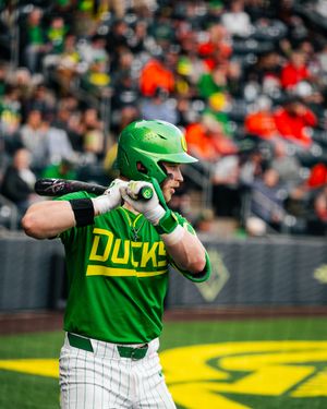 Oregon Ducks baseball player in green helmet and jersey stands at bat during a college baseball game.