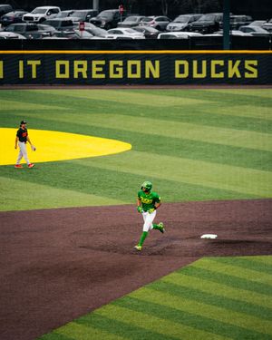 Oregon Ducks baseball player rounds the bases at PK Park during a home game on the vibrant green field.