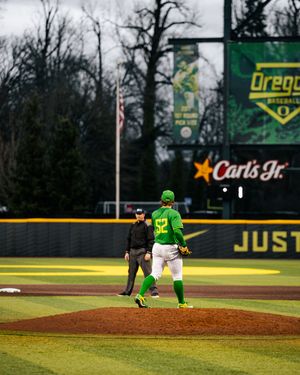 Oregon Ducks baseball pitcher #32 stands on the mound at PK Park with Carl's Jr. signage visible.