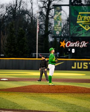 Oregon Ducks baseball pitcher stands on mound at PK Park during a game, with Carl's Jr. outfield signage visible.