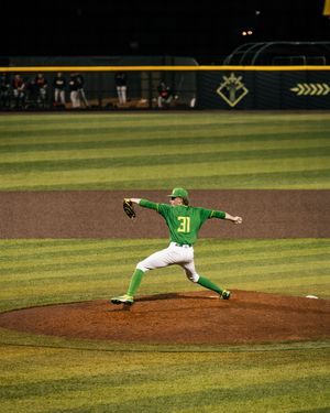 Baseball pitcher #31 in green uniform winds up to throw during a night game on a well-lit field.