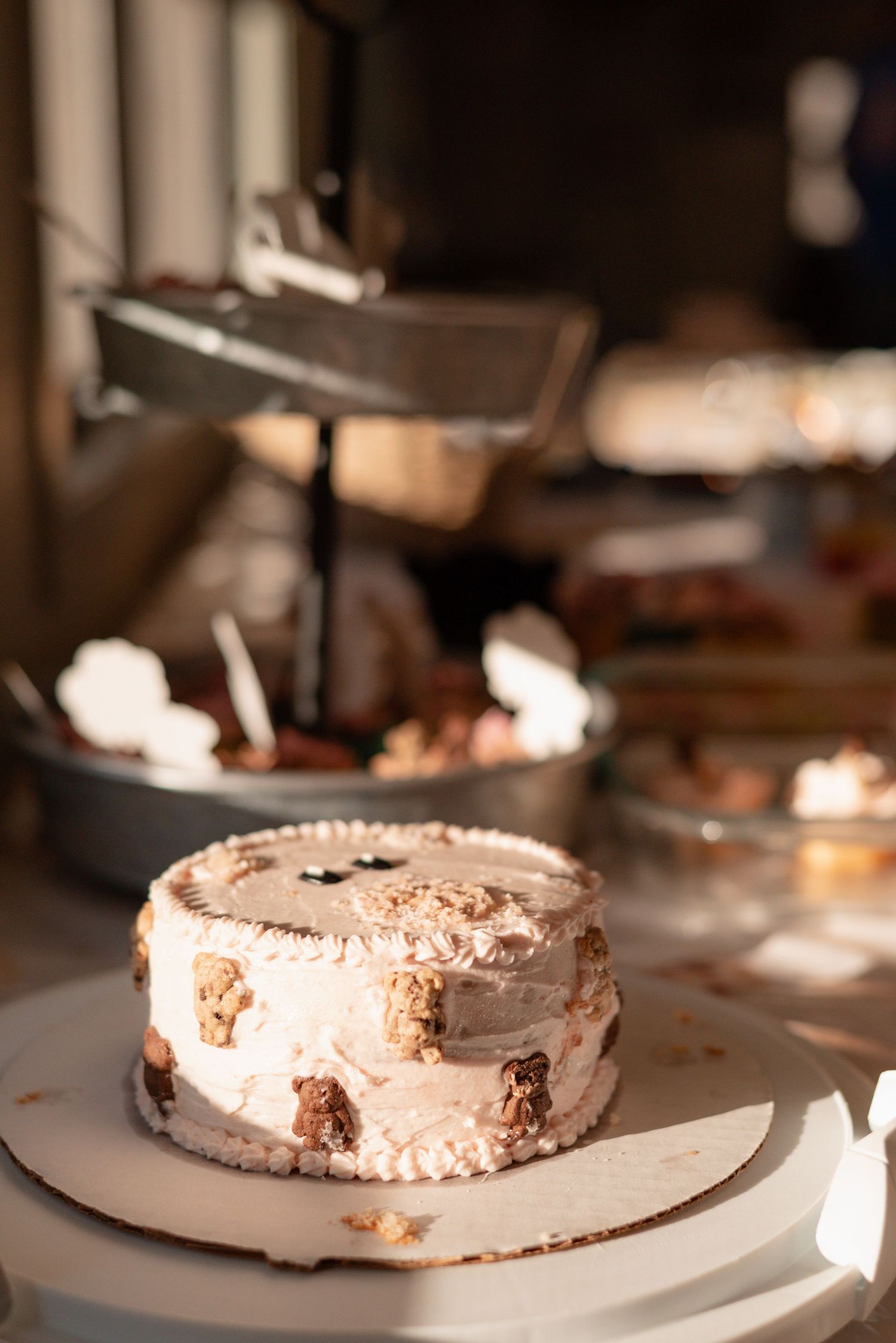 A decorated layer cake with cream frosting and candy toppings on a white cake stand at a dessert table.
