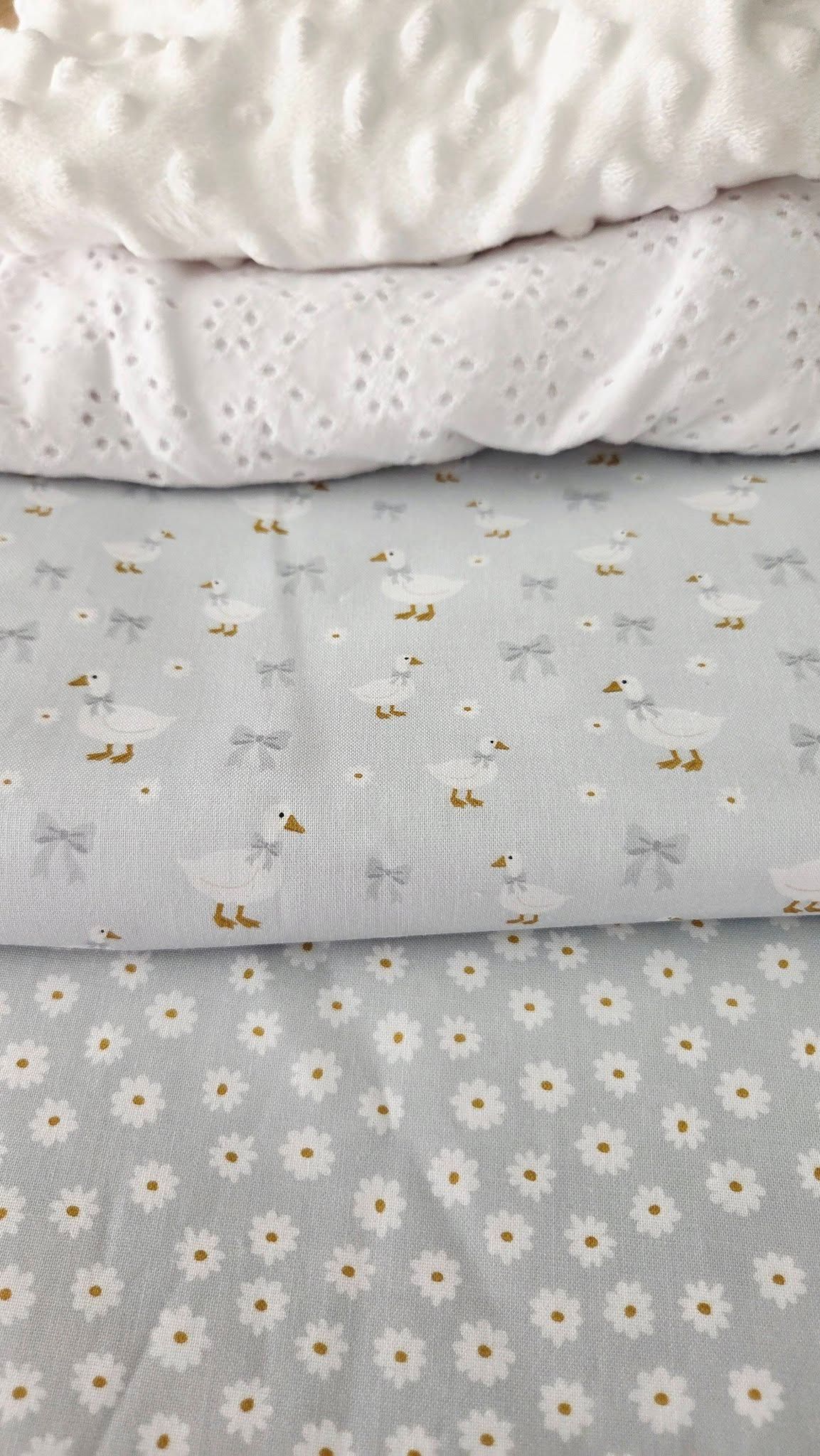 Stack of four baby fabrics: white minky dot, white eyelet, gray duck and bow print, and gray daisy print.