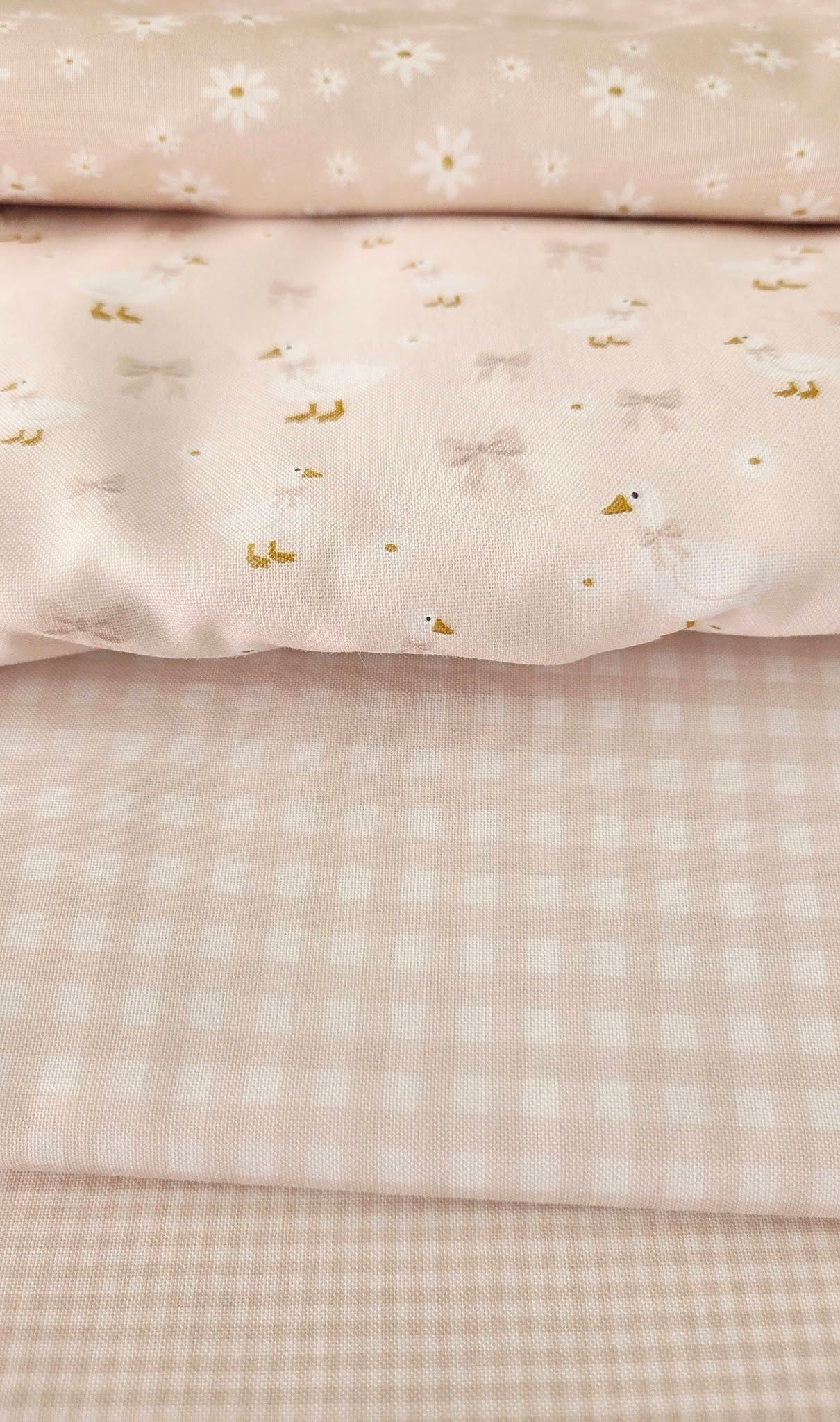 Stacked light peach fabrics with gingham, floral daisy, and duck bow prints for baby or nursery sewing projects.