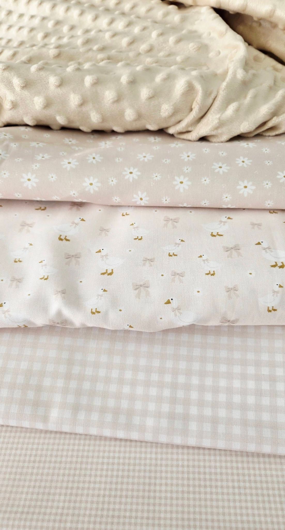 Stacked pastel pink baby fabrics featuring minky dot, daisy print, bow print, and gingham patterns.