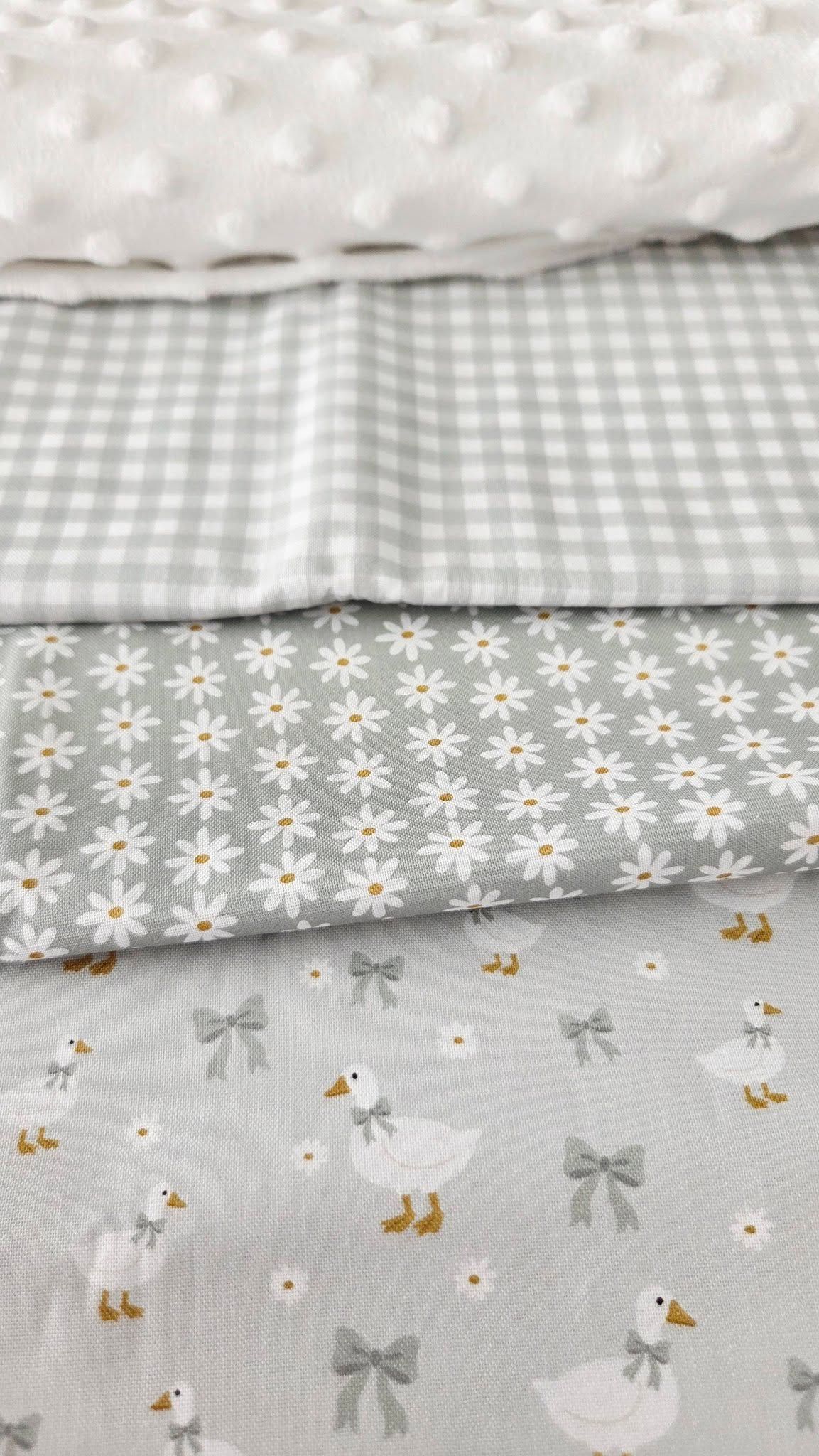 Gray baby fabrics stacked: white minky dot, gingham check, daisy print, and goose with bows pattern.