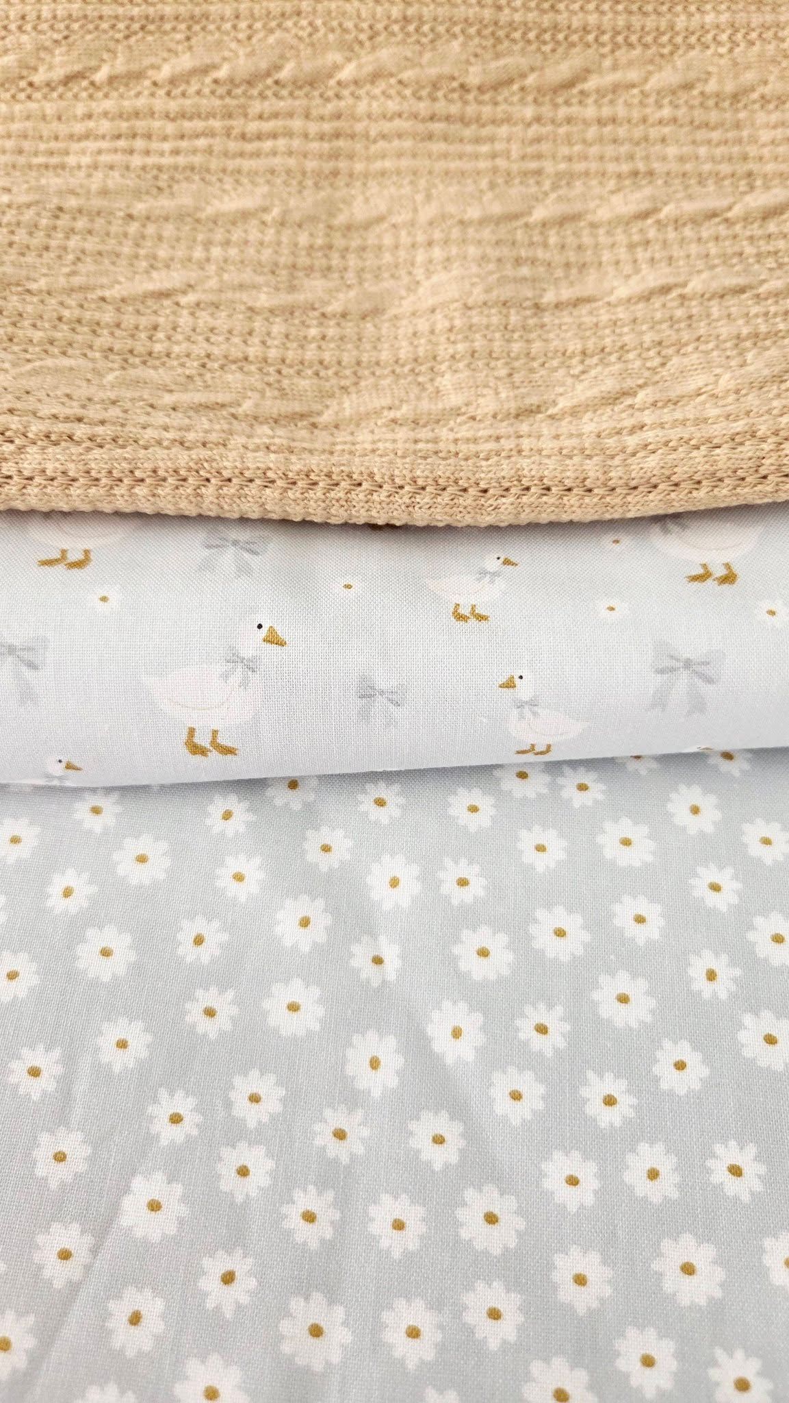 Three layered fabrics featuring a beige knit, white duck print, and white daisy pattern on light blue background.