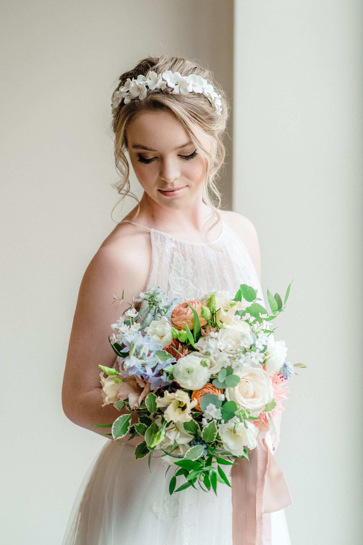 Elegant bride in white dress holding a pastel floral bouquet with roses and greenery, wearing a floral crown at Bull Point Estate.