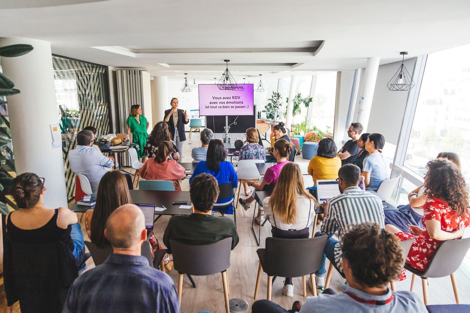 Audience attending a business presentation in a modern bright conference room with a purple screen display.
