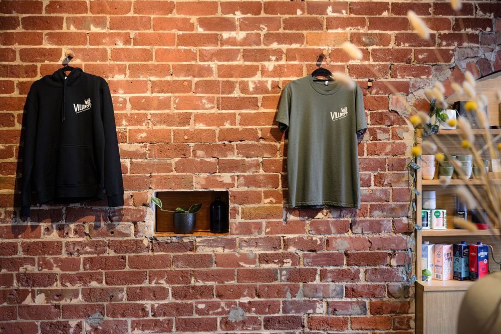 Two t-shirts displayed on hangers against rustic brick wall background.
