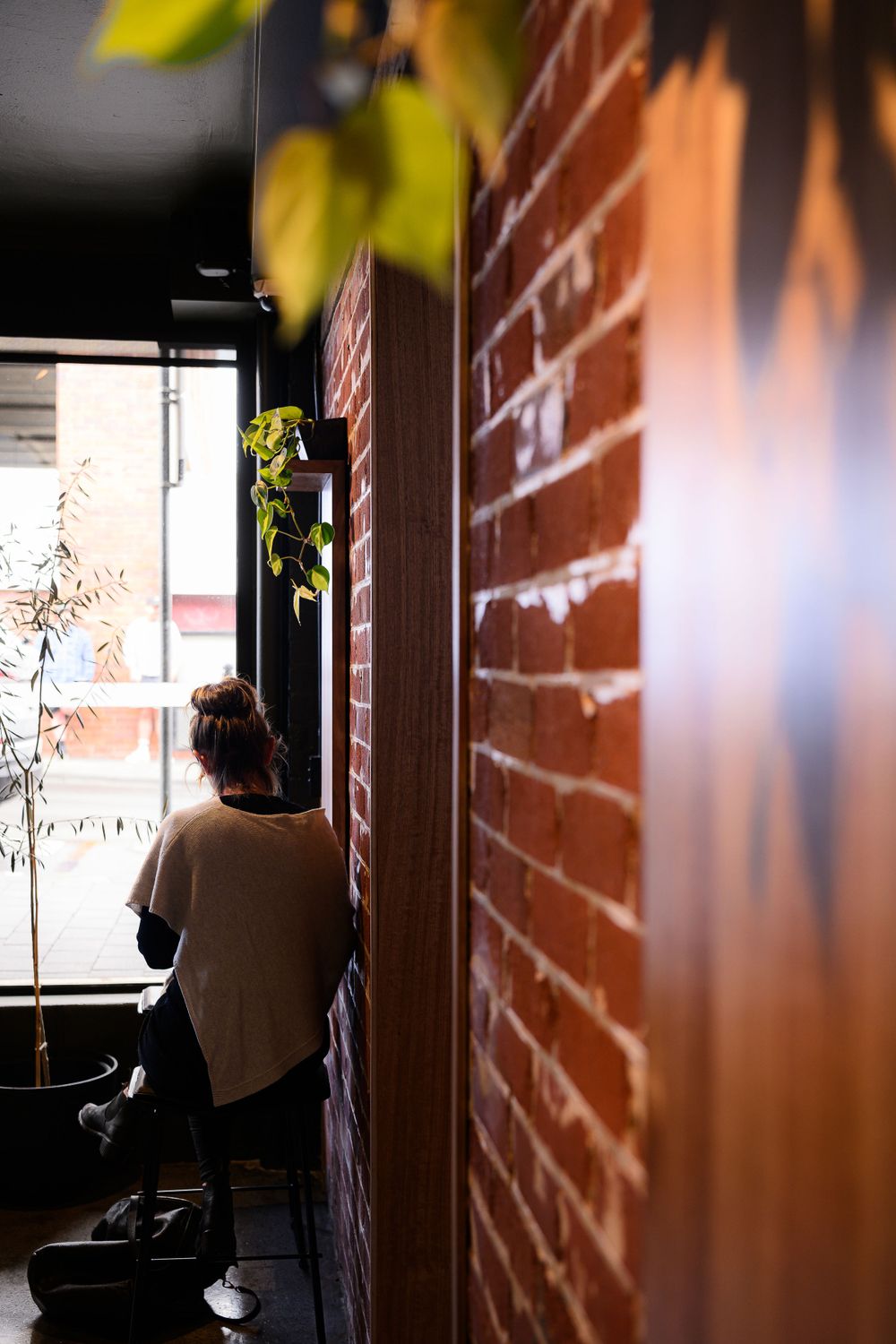 Sunlit interior scene with exposed brick wall and person sitting by window.