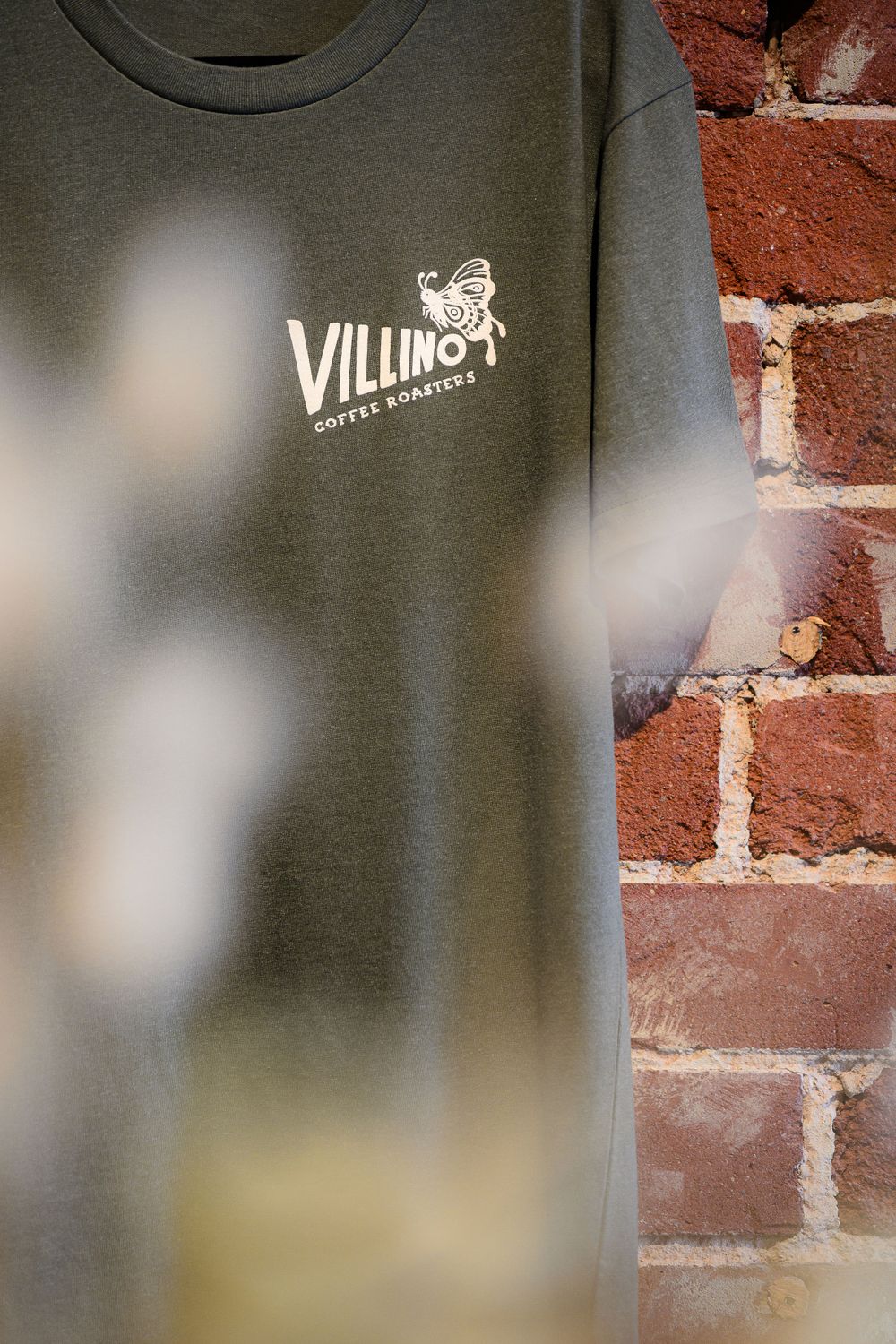 Close-up of a gray sweatshirt with Villino Coffee Roasters logo against a brick wall.
