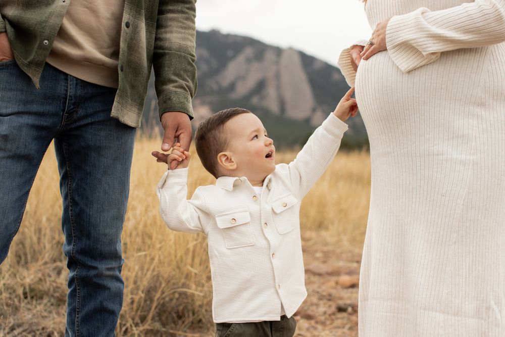 Small child in white shirt holds hands with caregivers while standing in a mountain field during sunset.